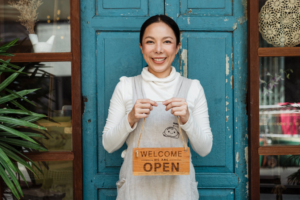 A small business owner posing with a welcome sign